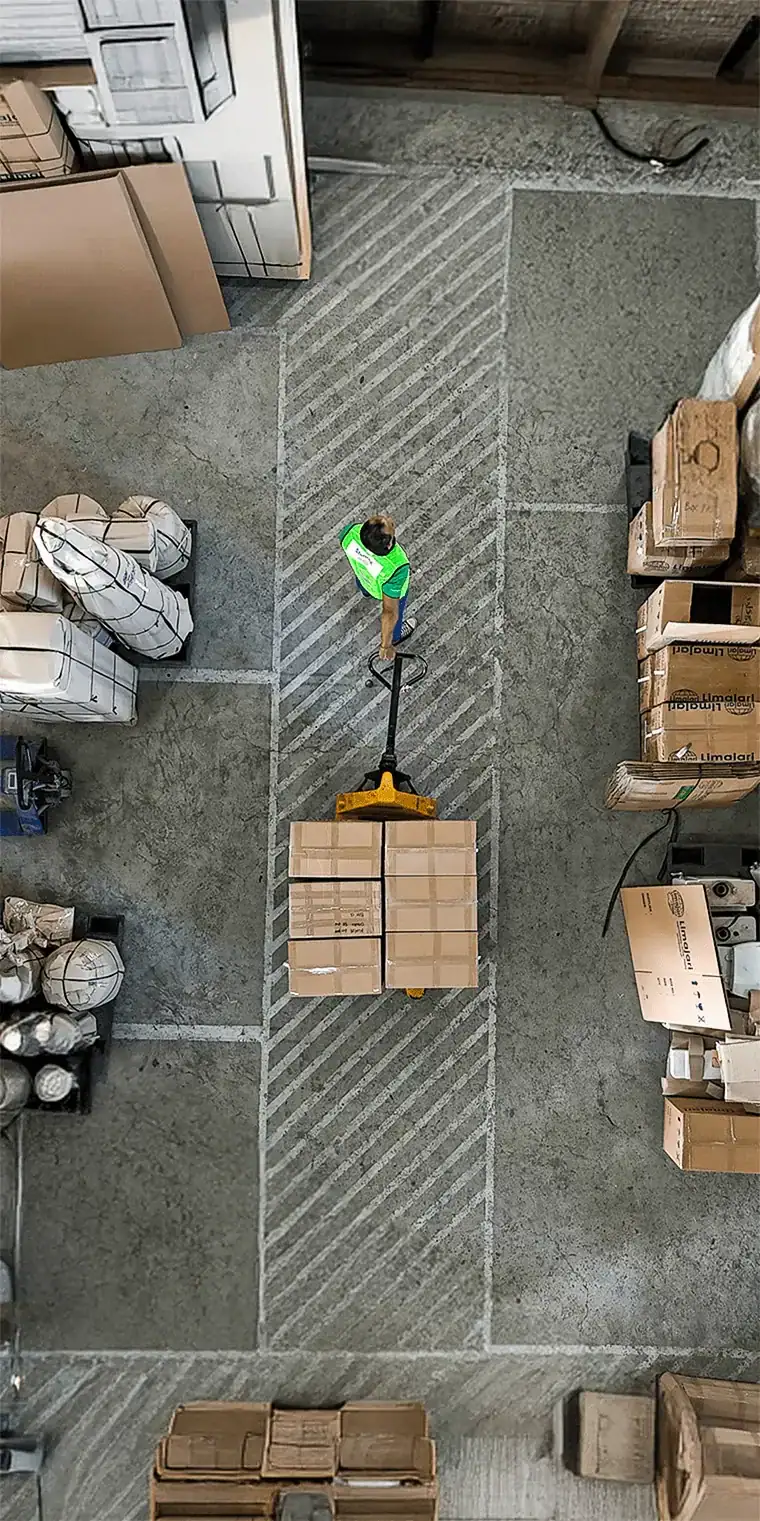 Vue aérienne d'un ouvrier gérant des marchandises dans un entrepôt avec des cartons et des palettes empilés.