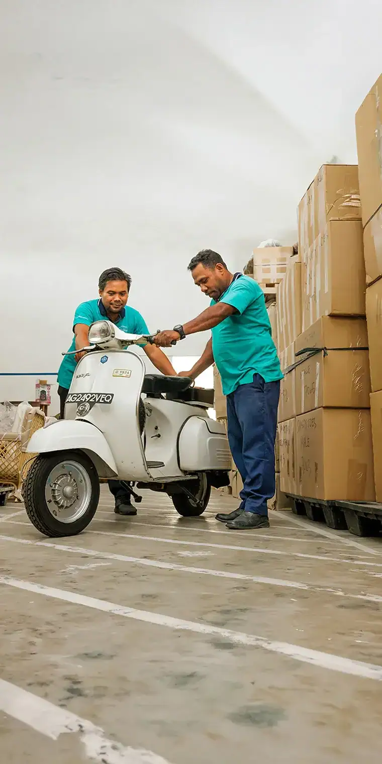 Une image présentant deux livreurs utilisant un scooter pour transporter des colis dans un entrepôt logistique. La scène met en avant la fiabilité de la manutention des marchandises et des services de transport.