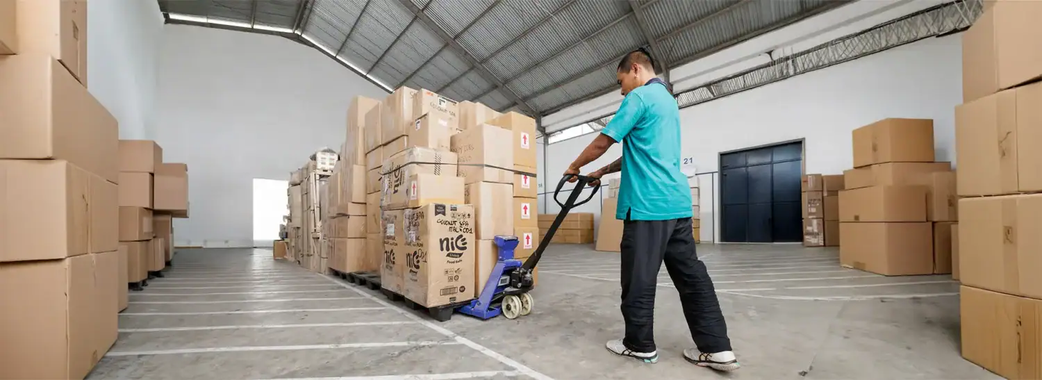Un employé utilisant un diable pour déplacer des cartons dans un entrepôt spacieux.
