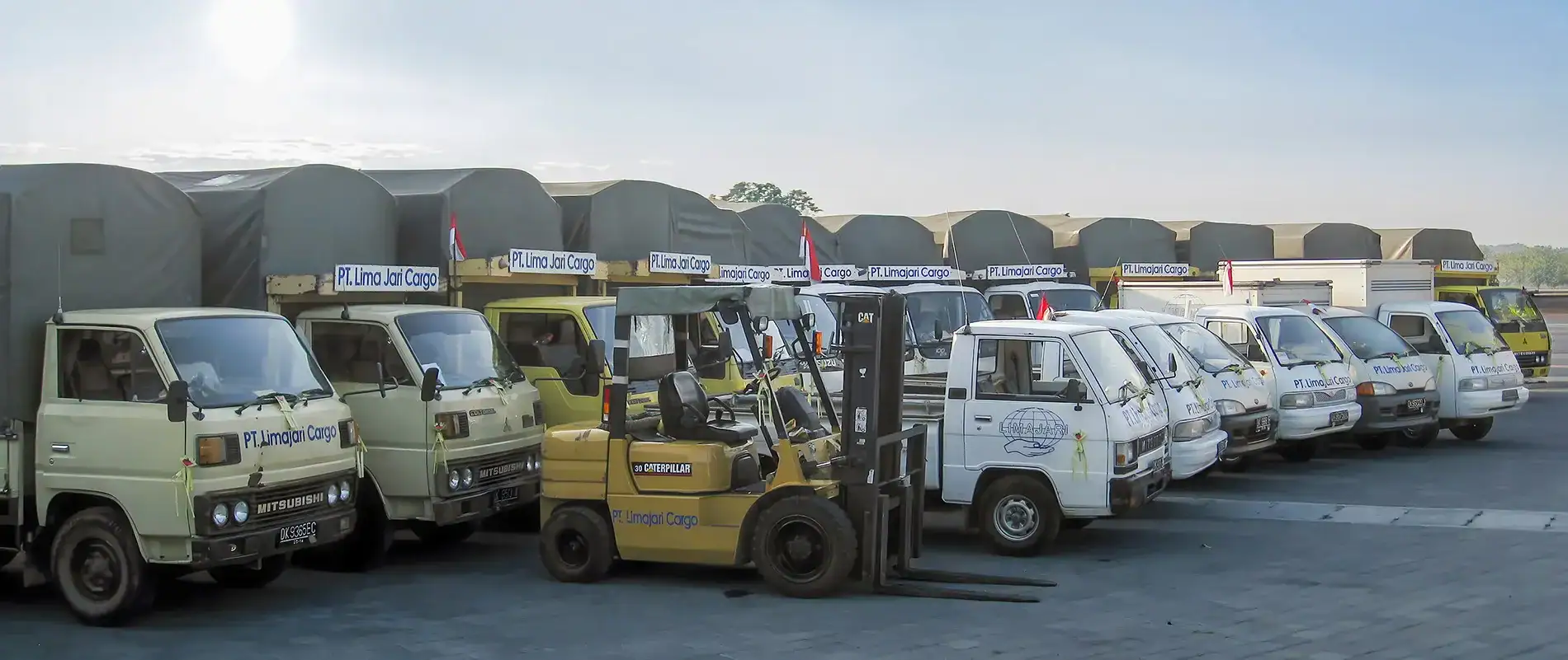 Fleet of cargo trucks and forklift at Limajari Cargo logistics yard, showcasing transportation and freight handling services.